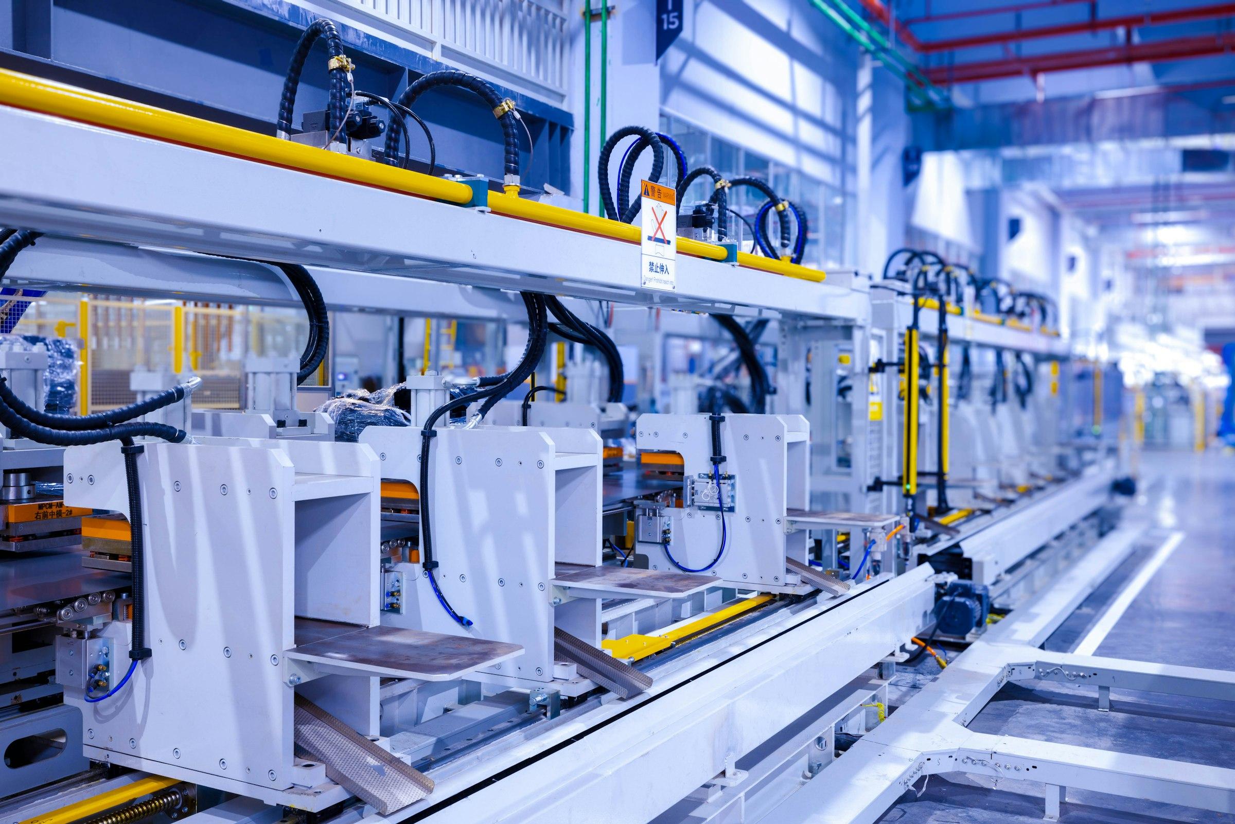 White-framed automated production line with guarded stations along a factory aisle