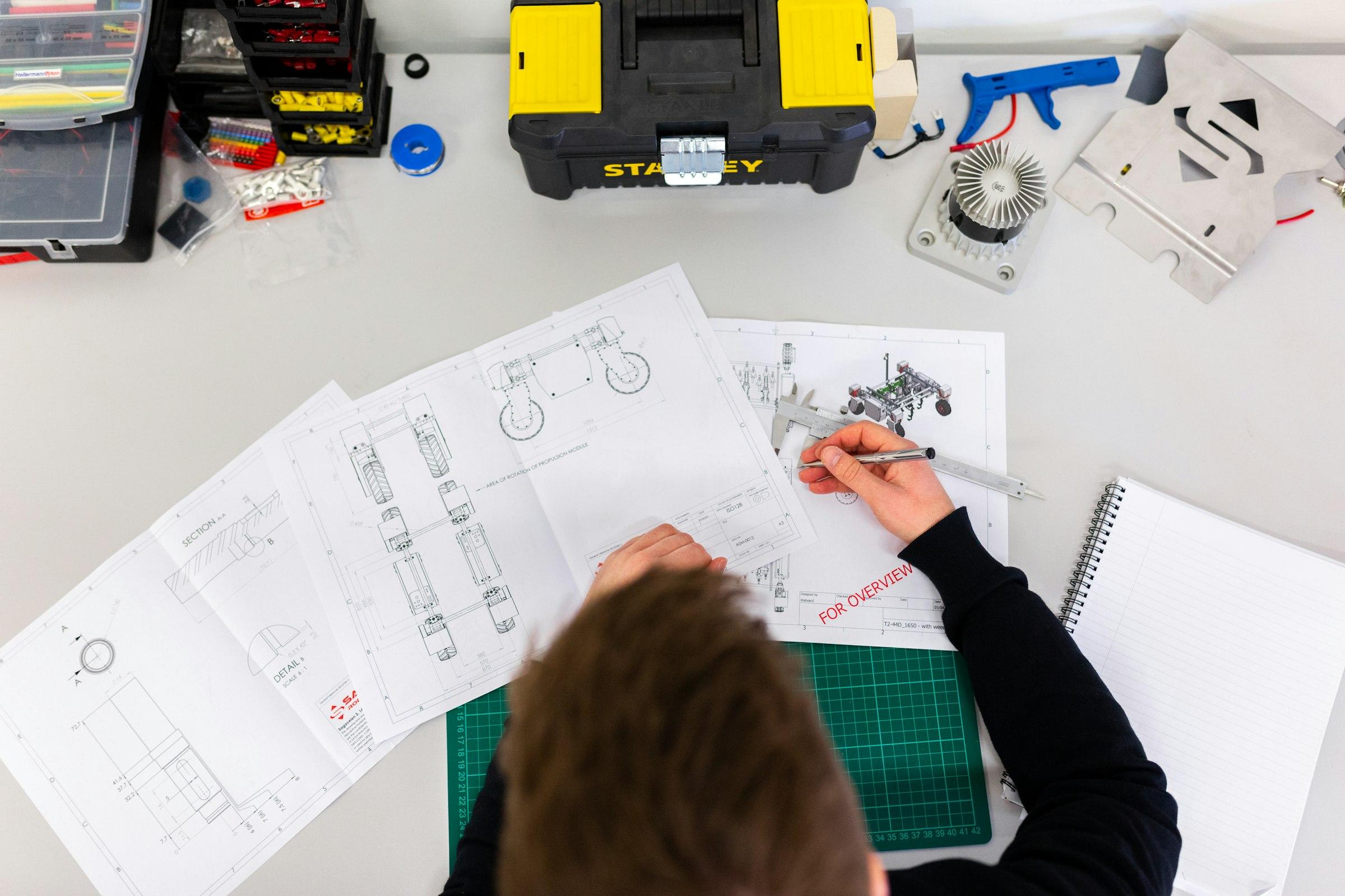 Engineer marking up printed mechanical drawings on a workbench beside tools