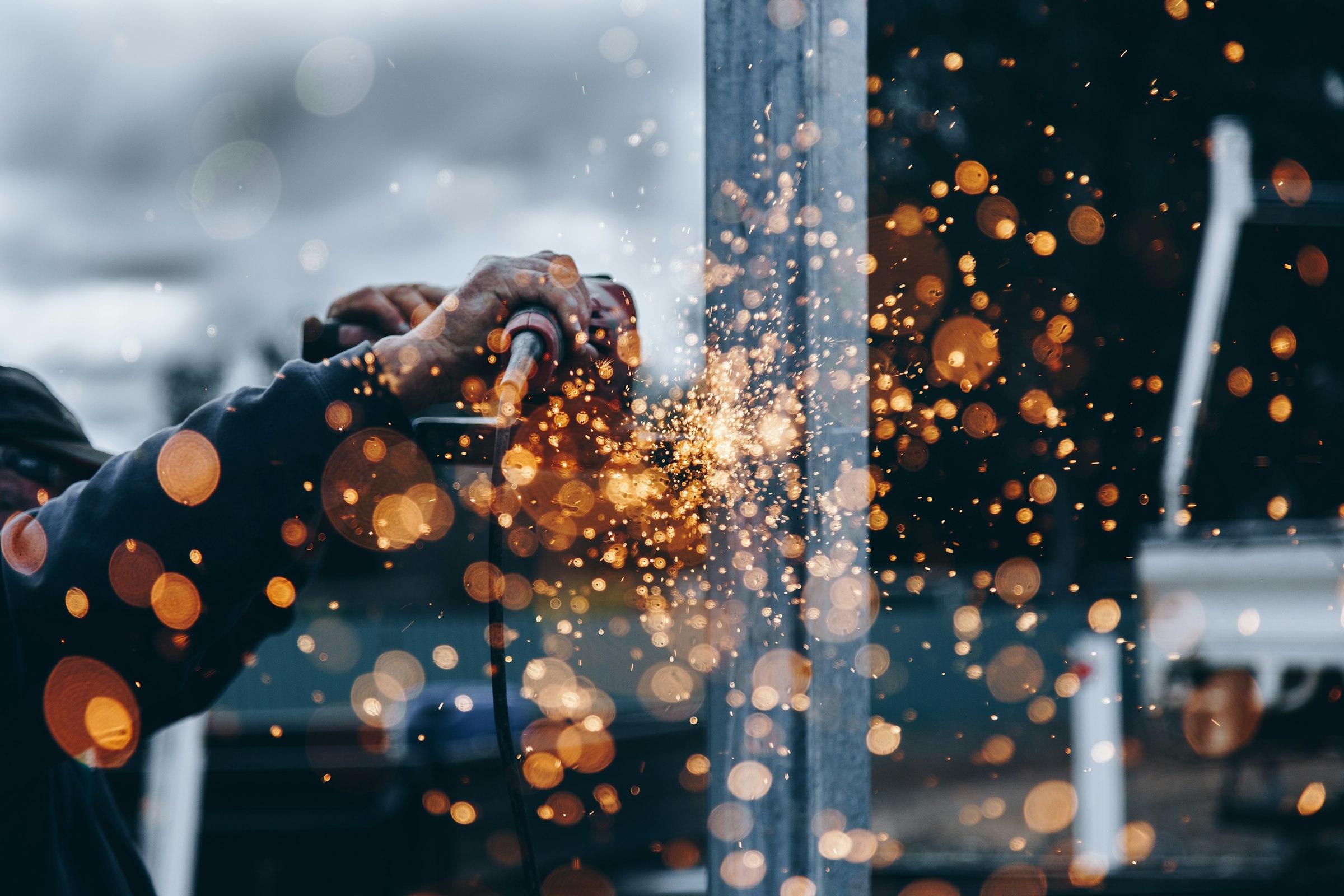 Technician grinding a steel component, sparks glowing against a dark workshop